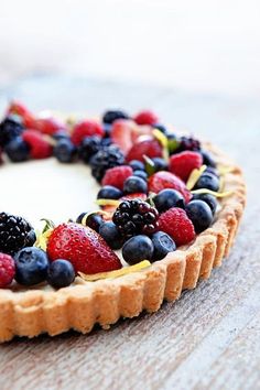 a fruit tart with berries and blueberries on top sits on a wooden table