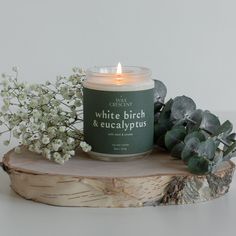 a candle sitting on top of a piece of wood next to flowers and greenery