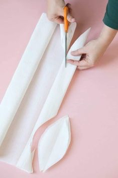 someone cutting paper with scissors on a pink surface