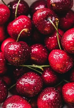 a bowl filled with lots of red cherries covered in water droplets on top of each other