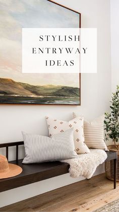 an entryway bench with pillows and a hat on it in front of a painting