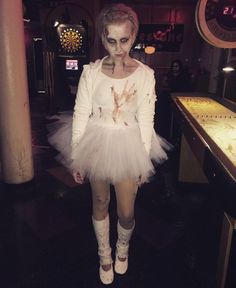 a woman dressed up as a zombie with white makeup and headdress, standing in front of a bar