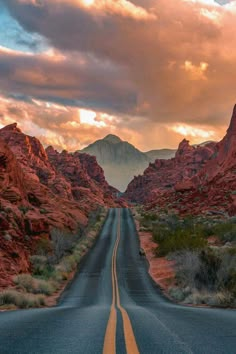 an empty road in the desert with mountains and clouds behind it at sunset or sunrise