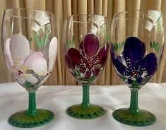 three wine glasses sitting on top of a table next to each other with flowers painted on them