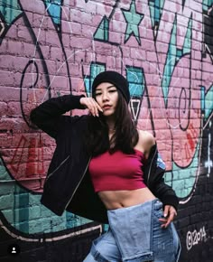 a woman standing in front of a brick wall wearing jeans and a cropped top