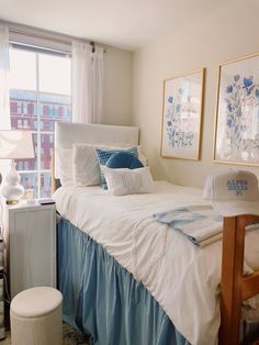 a white bed with blue and white pillows in a bedroom next to a large window