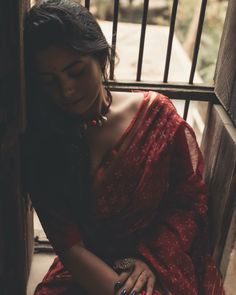 a woman in a red sari sitting on a wooden bench with her hands resting on her chest