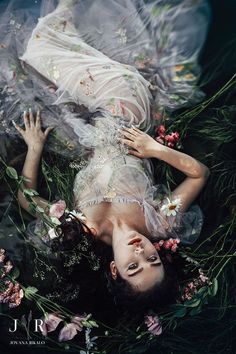 a woman laying on her back in the water surrounded by plants and flowers, wearing a white dress