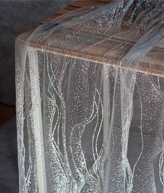 the sheer fabric is on top of the wooden table with silver sequins around it