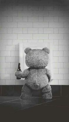 a large teddy bear standing in front of a white brick wall holding a beer bottle