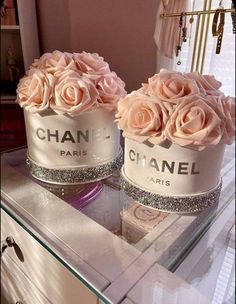 two chanel perfume bottles with pink roses in them sitting on a glass table next to a mirror