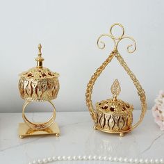 two gold jewelry pieces sitting on top of a white counter next to pearls and flowers