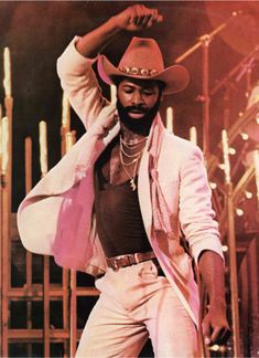 a man in a cowboy hat and white suit with his hands on his head, dancing