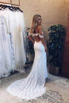 a woman standing in front of a mirror wearing a white wedding dress with off the shoulder sleeves