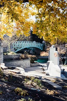 a blue bridge crossing over a river next to a park with trees in the foreground