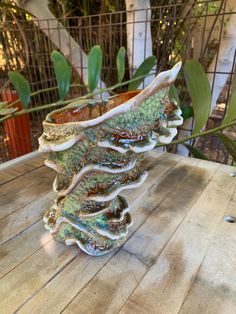 a ceramic vase sitting on top of a wooden table next to a planter and fence