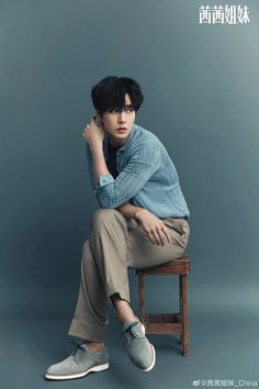 a man sitting on top of a wooden chair next to a blue wall with his hand under his chin