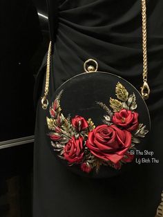 a black purse with red roses on it and gold chains hanging from the front pocket