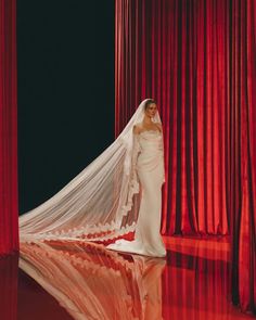 a woman in a white wedding gown and veil standing on a stage with red curtains