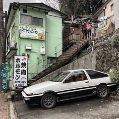 a white car parked on the side of a road next to a green building and stairs