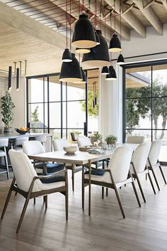 a dining room table with chairs and lights hanging from it's ceiling, in front of large windows