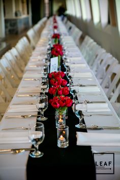 the long table is set with white chairs and red flowers in vases on each side