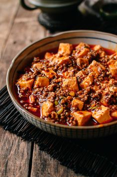 a bowl filled with chili and tofu on top of a wooden table next to other dishes