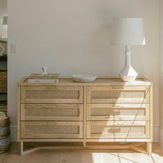 a white lamp sitting on top of a wooden sideboard next to a dresser with drawers