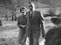 an old black and white photo of two people standing in the grass near some bushes