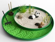 a green tray with rocks and plants in it on a white surface, including two pandas