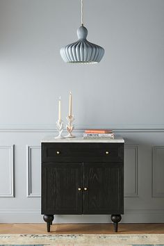 a black cabinet with two candles on top and a blue light hanging from the ceiling