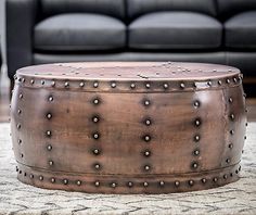 a large round metal ottoman sitting on top of a rug in front of a couch