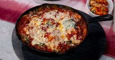 a pizza in a skillet on a table with other dishes around it and a red striped table cloth