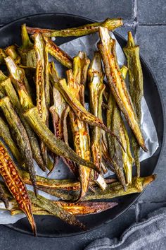 grilled green beans in a black bowl on a gray tablecloth, top view