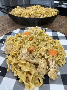 two plates with food on them sitting on a table next to a skillet filled with chicken and noodles