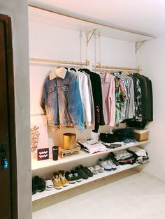 an open closet with clothes and shoes hanging on the wall next to a shelf filled with other items