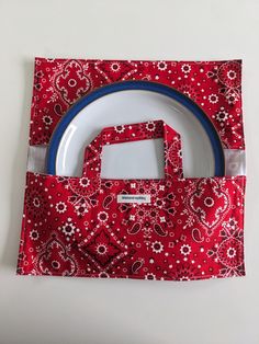 a red bag with white and blue trim on top of it next to a plate