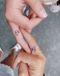 two people holding hands with tattoos on their fingers and one has a flower tattoo on the middle finger