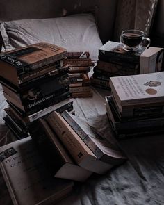 a pile of books sitting on top of a bed next to a glass of wine