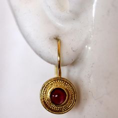 Handcrafted of a tiny disc of filigree thread, this classic Greek design highlights the beauty of a single cabochon garnet. The original Greek earrings are part of the Museum's permanent collection. 14k gold settings. Hinged backs for pierced ears. Size: 7/8 Inches. Elegant Gold Garnet Cabochon Jewelry, Byzantine Jewelry With Cabochon For Gifts, Byzantine Cabochon Jewelry For Gifts, Byzantine Style Cabochon Jewelry For Gifts, Byzantine Style Cabochon Jewelry Gift, Yellow Gold Garnet Round Earrings, Round Cabochon Garnet Jewelry, Round Garnet Cabochon Jewelry, Gold Ruby Round Earrings