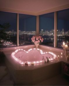 a bathtub with candles and flowers in front of a large window overlooking the city