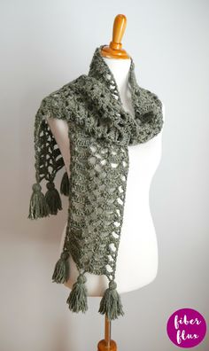 a white mannequin wearing a green crocheted scarf with tassels