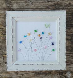 a white frame with flowers and butterflies in it on a wooden table next to a piece of wood