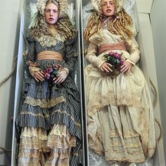 two women dressed in victorian clothing laying on their stomachs next to each other and holding flowers