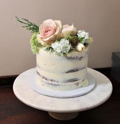 a white cake with flowers and greenery on top sits on a table in front of a wall