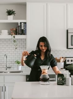 a woman pours coffee into a pot on the kitchen counter, surrounded by white cabinets