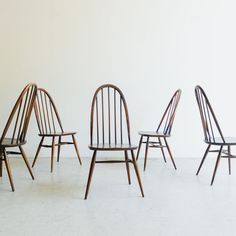 four wooden chairs sitting next to each other on a white floor in front of a wall