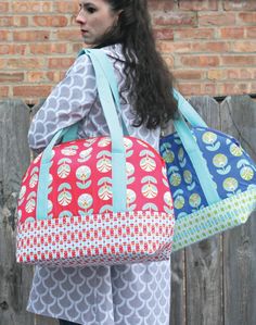 a woman carrying a large colorful bag on her back while standing in front of a brick wall