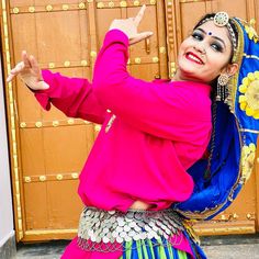 a woman dressed in colorful clothing standing next to a wooden door with her arms outstretched