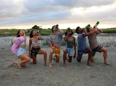 a group of people standing next to each other on top of a sandy beach with bottles in their hands